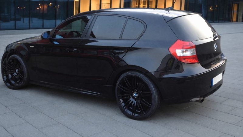 Schwarzer BMW 1er mit Tönungsfolie Tiefschwarz vor einer Glasfassade am Abend