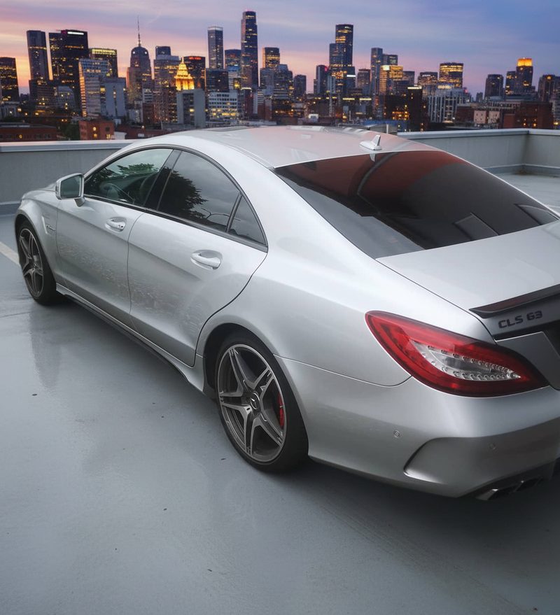Silberner Mercedes CLS mit getönten Scheiben auf einem Parkdeck vor der Skyline